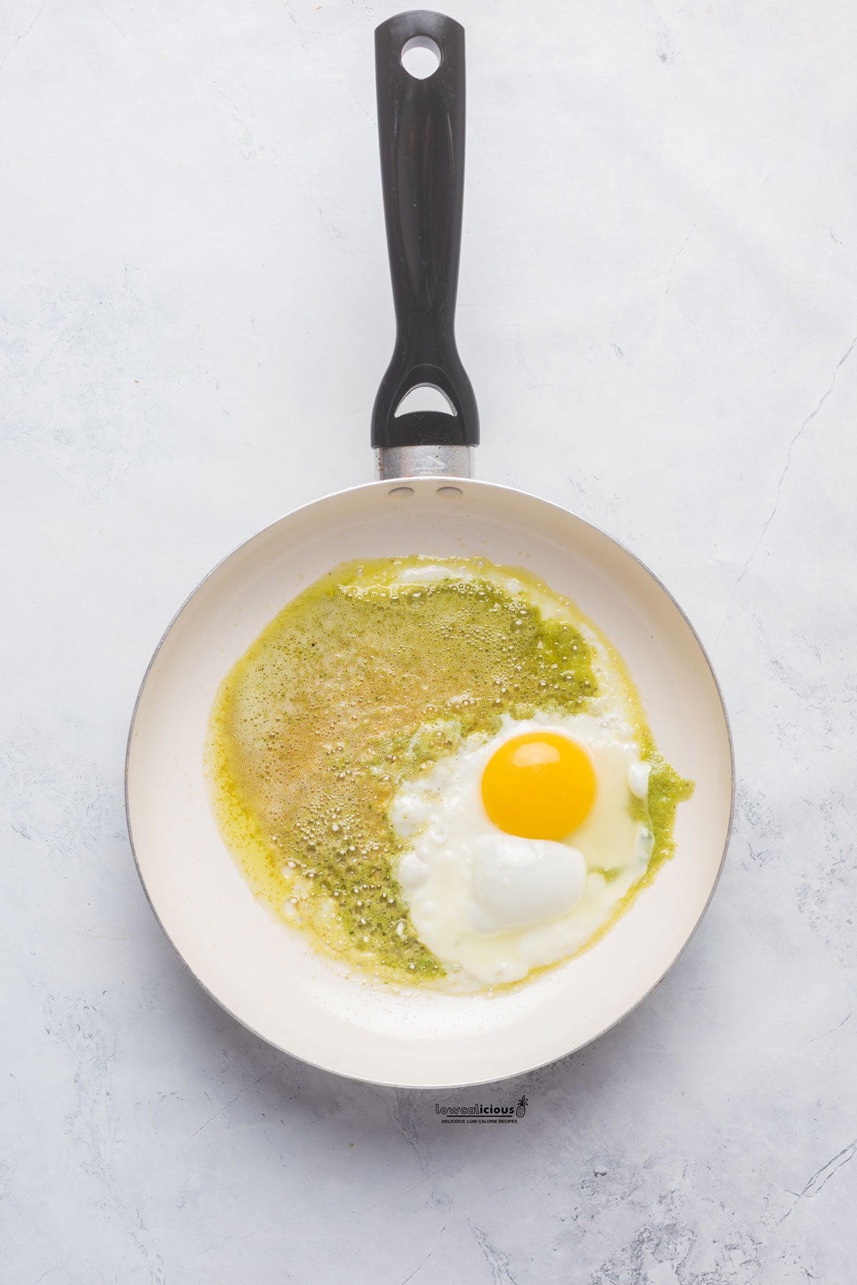 a nonstick skillet with pesto and an egg cooking in it to make Pesto Eggs (Viral TikTok Recipe)