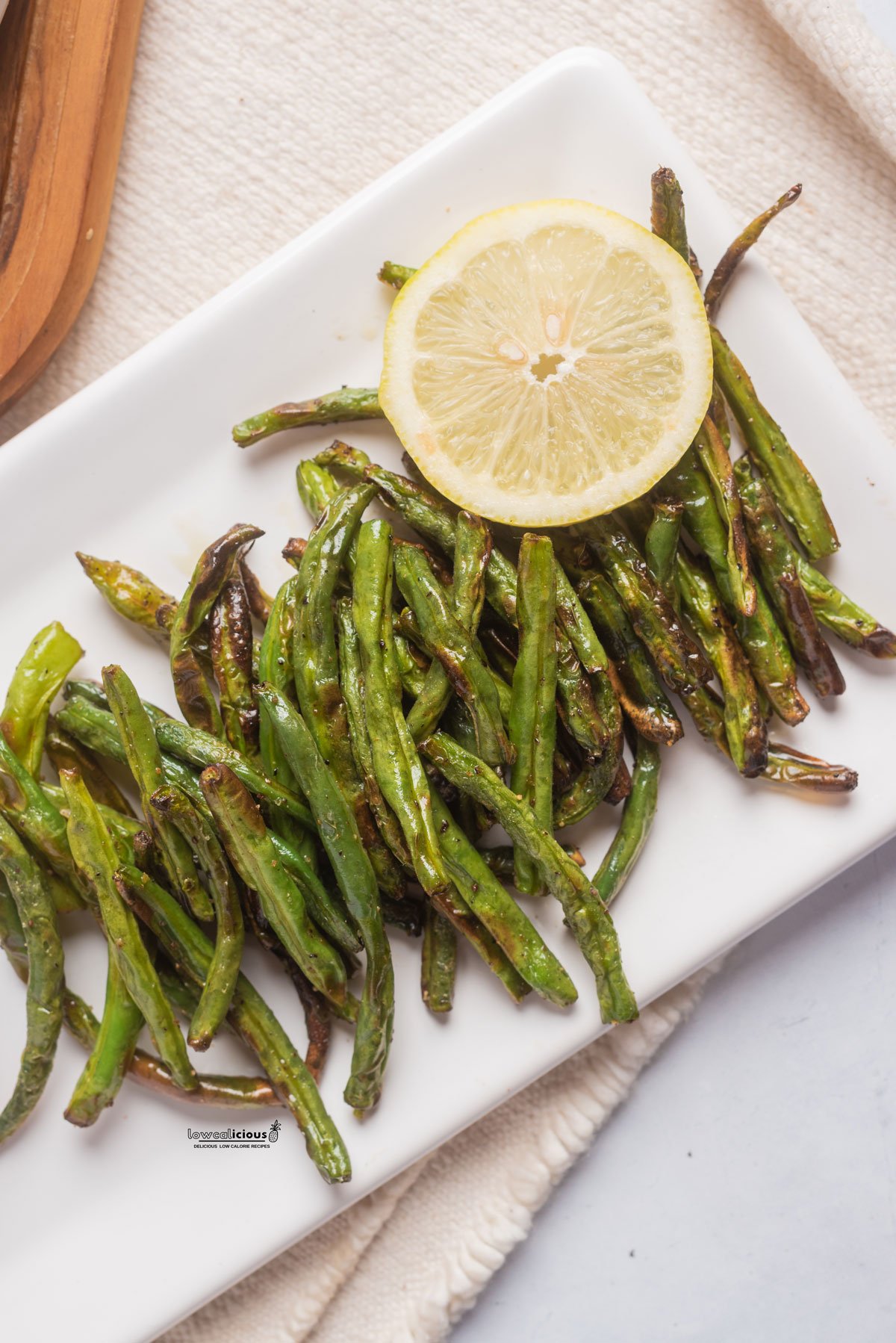 cooked air fryer green beans on a white rectangle platter with a wheel of lemon on top