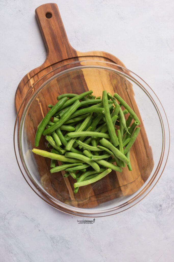 fresh green beans in a clear glass bowl on a wood cutting board ready to be seasoned