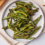 cooked air fryer green beans on a round white plate on top of a white napkin ready to serve