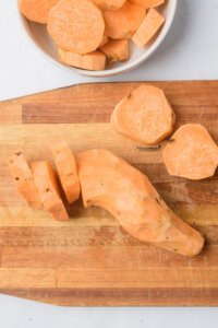 sliced sweet potatoes on a wood cutting board to make Viral Smashed Sweet Potatoes (Air Fryer Recipe)