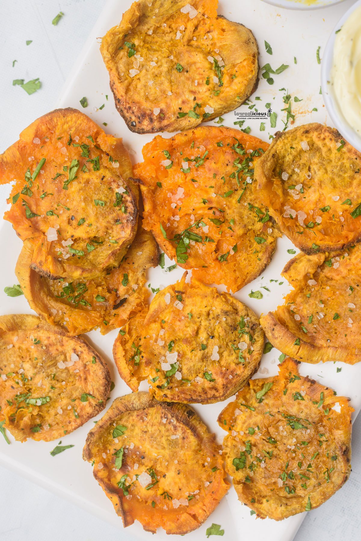 overhead shot of cooked Viral Smashed Sweet Potatoes (Air Fryer Recipe) plated on a white platter and topped with chopped fresh parsley
