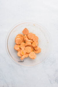 sliced sweet potatoes in a glass bowl coated in spices and olive oil to make Viral Smashed Sweet Potatoes (Air Fryer Recipe)