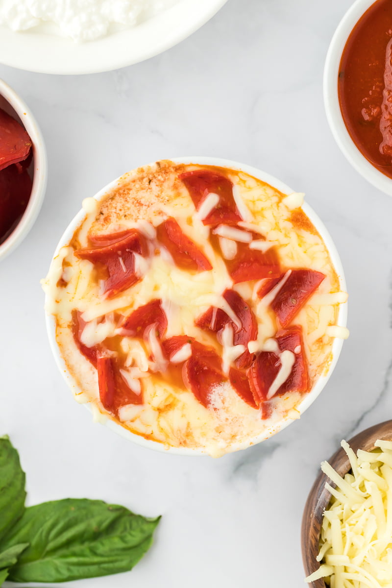 overhead shot of a cooked cotttage cheese pizza bowl topped with melted cheese and diced pepperoni in a small white ramekin