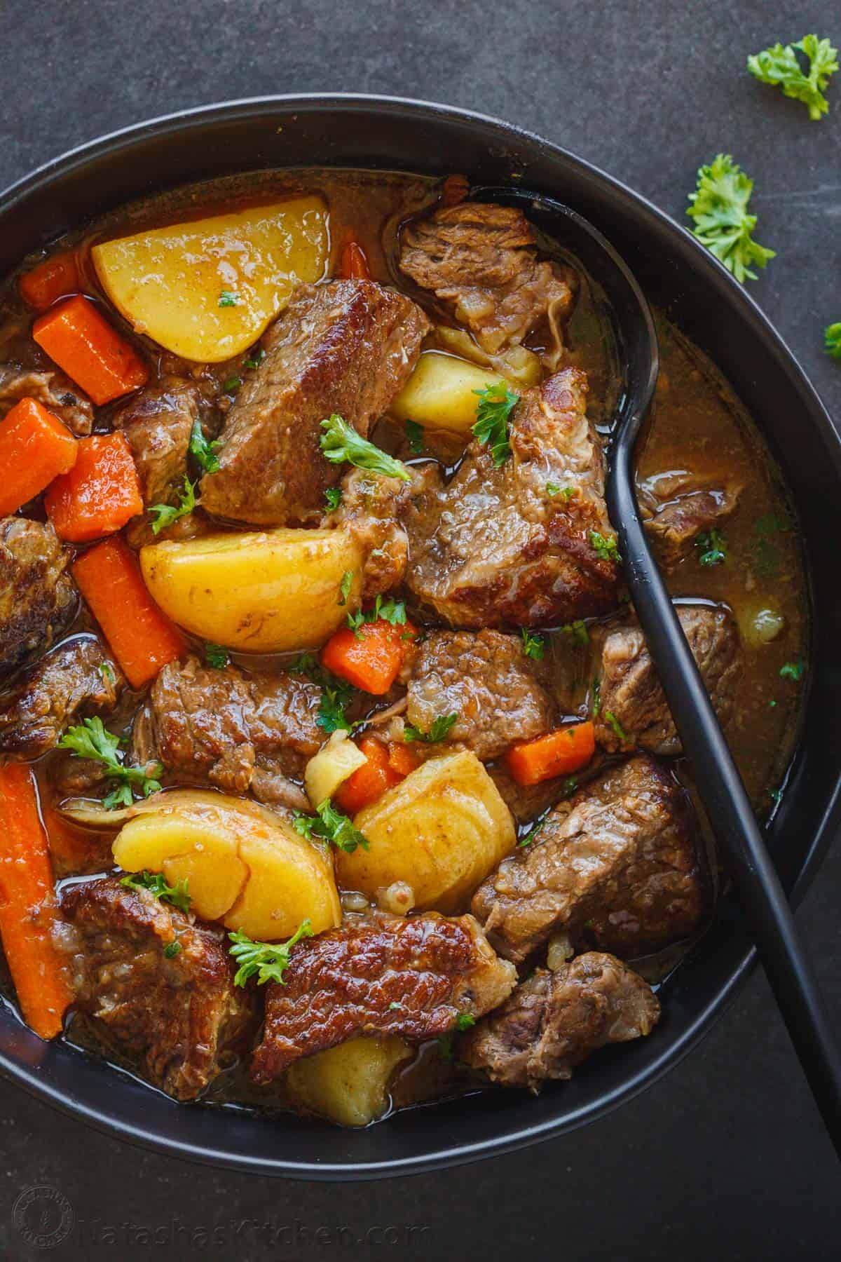 healthy slow cooker beef stew in a black bowl with a black spoon on a dark gray surface - one of the recipes for this week's healthy weekly meal plan