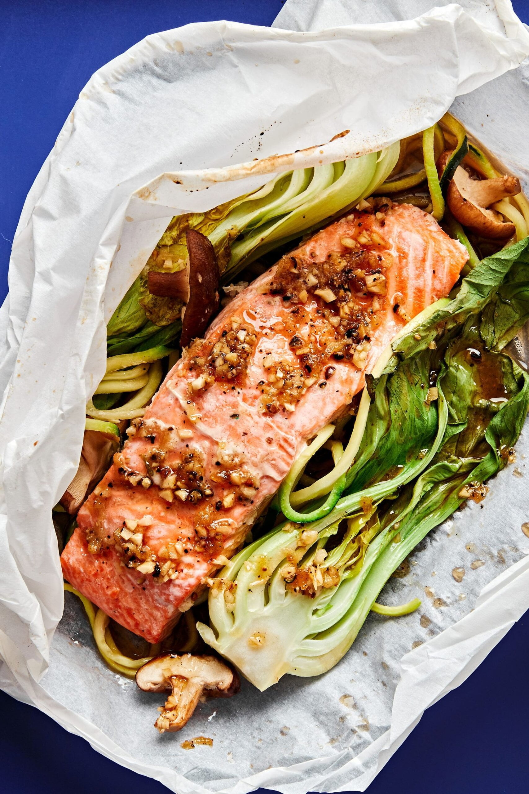 Garlic Ginger Salmon with Zoodles cooked in a white parchment paper packet on top of a cobalt blue surface