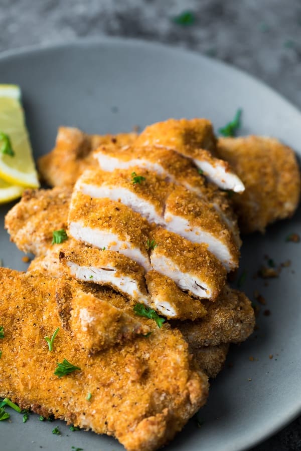 cooked and sliced crispy air fryer chicken breast on top of a plate of more pieces of cooked chicken breast coated in breadcrumbs
