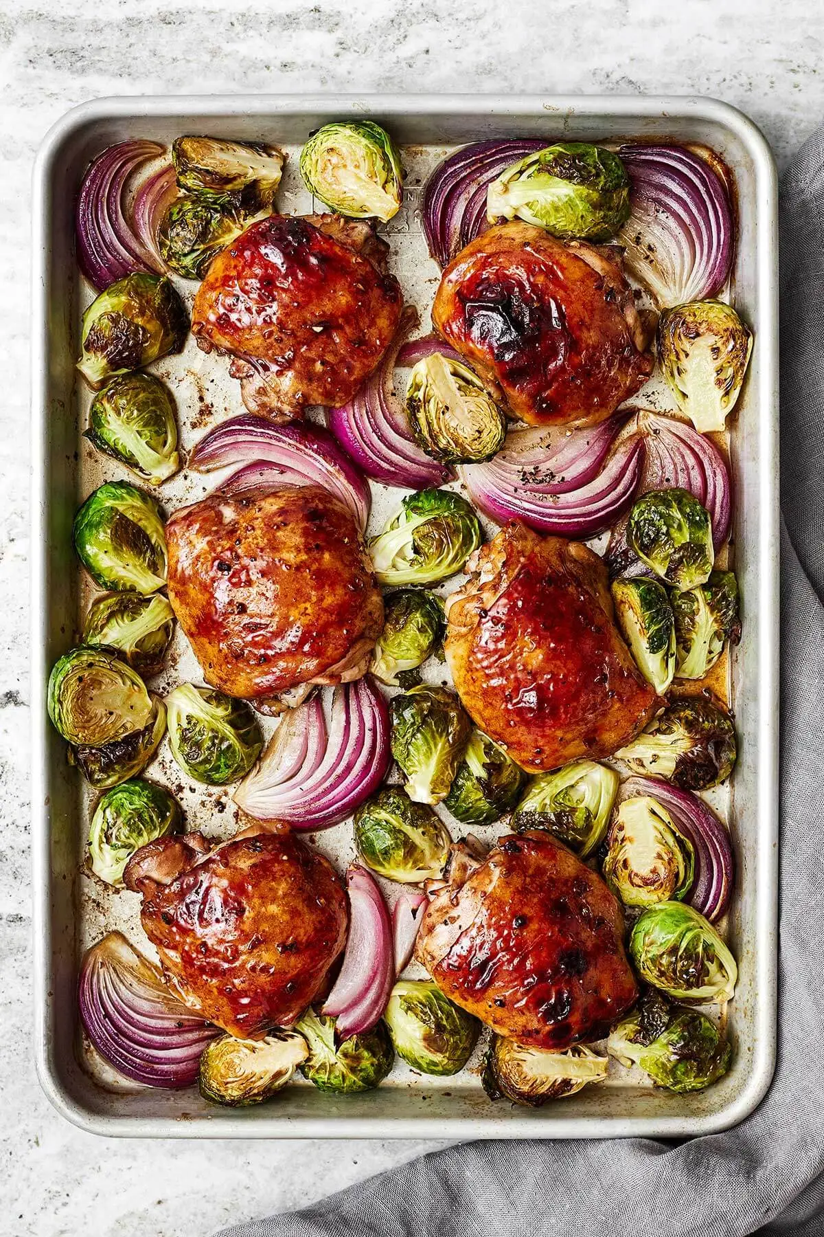 overhead shot of cooked Balsamic Chicken and Brussels Sprouts with red onion on a rimmed sheet pan - one of the recipes for this week's healthy weekly meal plan