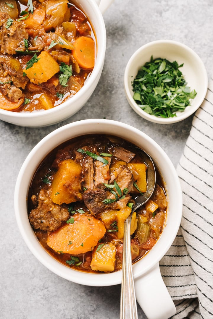 two bowls of Whole30 Beef Stew in a white bowls garnished with chopped fresh parsley - one of the recipes for this week's healthy weekly meal plan