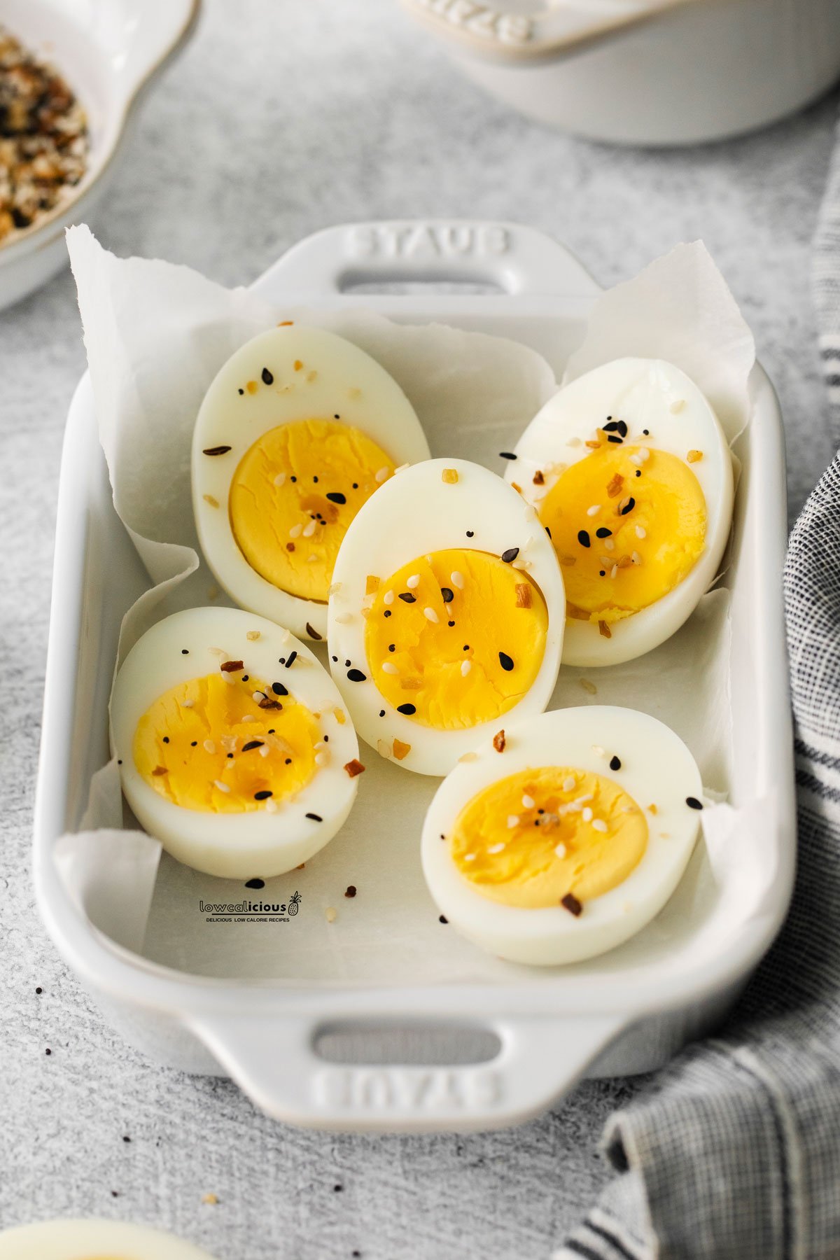 cooked Air Fryer Hard Boiled Eggs in a white parchment paper lined small white rectangular Staub dish seasoned with everything bagel seasoning