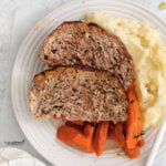 cooked healthy Air Fryer Meatloaf plated on a round white plate with mashed potatoes and roasted carrots.