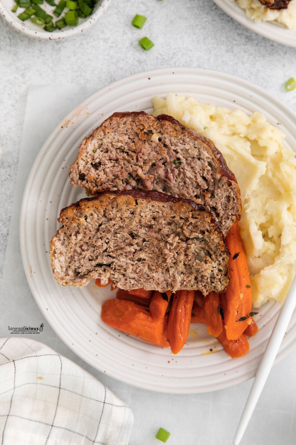 cooked healthy Air Fryer Meatloaf plated on a round white plate with mashed potatoes and roasted carrots.