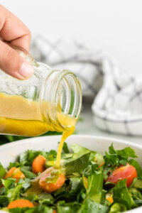 homemade vinaigrette in a clear jar being poured over a fresh garden salad