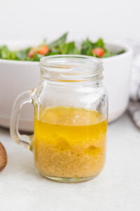 ingredients to make a homemade vinaigrette in a clear glass mason jar with a handle.